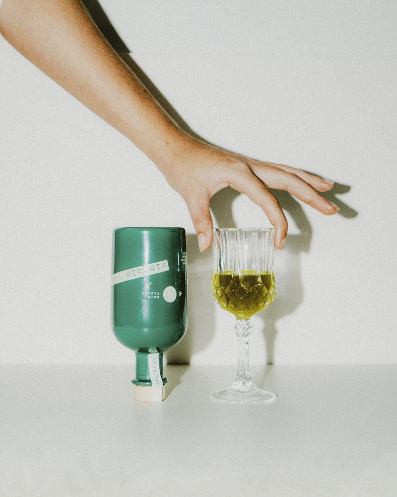 Una mano deja la botella Símbolo junto a una copa llena de aceite de oliva virgen extra