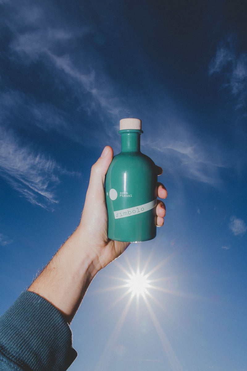 Una mano sostiene la botella de AOVE contra el cielo: cabe en la palma