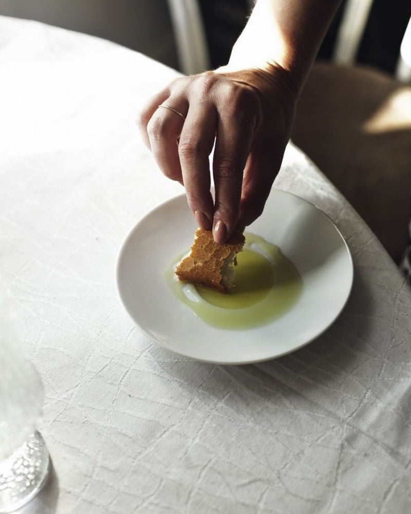 Una mano moja pan en un cuenco de aceite de oliva virgen extra